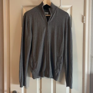 Grå cardigan kofta med dragkedja från pier one - Säljer en stilren grå kofta från pier one med hel dragkedja framtill och ribbad krage. Tröjan har långa ärmar, fickor på sidorna och är tillverkad i mjukt material som passar perfekt till lager-på-lager. Enkel och clean look för alla tillfällen.