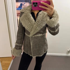 Beige pälsjacka med bred krage - Säljer en beige pälsjacka med bred fluffig krage och muddar. Jackan har markerade sömmar och är figursydd med omlottstängning. Pälsen är mjuk och jackan har en snygg vintagekänsla. Perfekt skick
