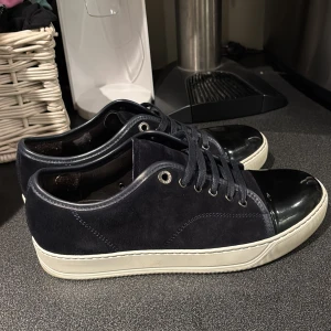Lanvins - Snygga mörkblå sneakers från Lanvin med ovandel i mocka och detaljer i skinn. Tåpartiet är i svart lack och sulan är vit. Skorna har snörning och klassisk låg profil. Perfekta för dig som gillar stilrena och exklusiva sneakers med en twist. Dessa är köpta nya och använda 5 gånger. Uk5 och passar 40-41-42. Pris kan diskuteras vid snabb affär 