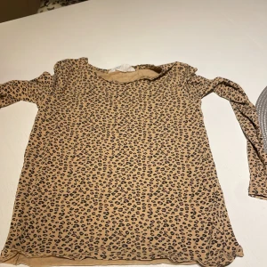 Leopardmönstrad långärmad tröja H&M - Säljer en beige långärmad tröja från H&M med coolt leopardmönster. Tröjan har en klassisk rund halsringning och är tillverkad i mjukt material som är skönt mot huden. Perfekt för dig som vill sticka ut lite extra med din outfit.