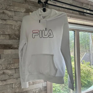 Vit hoodie från FILA  - Säljer en vit hoodie från FILA i storlek S. Tröjan har stor broderad FILA-logga på bröstet, huva med snörning och en stor magficka. Perfekt för dig som gillar sportig och clean stil.