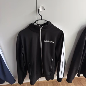 Palm Angels Zip Tröja - Säljer nu min svarta Palm Angels tröja då jag har tröttnat på den. Tröjan är i totalt nyskick och är 100% autentisk (bild på CLG kod skickas vid intresse). Storleken är M. 😊priset är ej hugget i sten:)