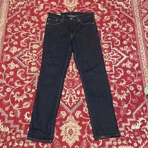 Levi's 511 - Säljer ett par Levi's 511 jeans i mörkblå denim. Modellen är slim fit med klassiska fem fickor, gul kontrastsöm och läderpatch bak i midjan. Perfekta för dig som gillar en smalare passform och stilren look.