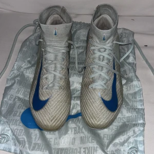 Nike mercurial superfly 10 elite fotbollskor   - Priset går å diskutera vid snabb affär Säljer ett par Nike Air Zoom fotbollsskor i beige med blå detaljer och snörning. Skorna har en högre strumpliknande krage och platt sula med dobbar för extra grepp på planen. Materialet är syntet och mesh för lätthet och ventilation. Medföljer en matchande beige/blå Nike-påse.
