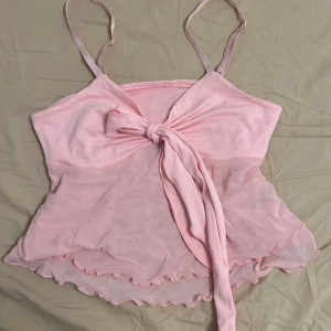 Rosa omlott linnetopp med knyt - Supersöt ljusrosa linnetopp med tunna axelband och stor knytrosett framtill. Perfekt sommartopp 💕