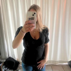 Svart ribbad topp med puffärm KappAhl - Svart ribbad topp från KappAhl med v-ringning och korta puffärmar. Snygg, figurnära passform och stretchigt material som sitter skönt. Perfekt till jeans eller kjol för en trendig look.