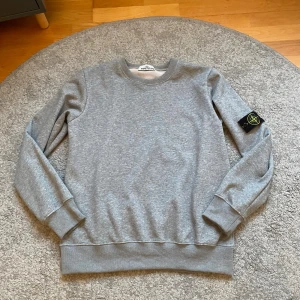 Stone Island sweatshirt - Grå sweatshirt från Stone Island med loggan på vänster ärm. Nyskick då den inte kommit till så mycket andvändning. Priset är förhandlingsbart, hör gärna av dig vid frågor eller funderingar.