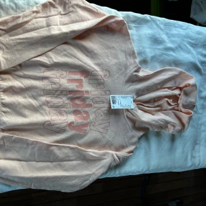 Ljusaprikos hoodie med tryck 'friday' - Säljer en ljust aprikos hoodie från H&M med coolt 'friday' tryck på framsidan. Tröjan är kort, har huva, långa ärmar och är gjord i mjuk bomull och polyesterblandning. 
