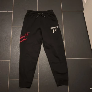 Svarta mjukisbyxor från Hoodrich  - Jag säljer ett par helt oanvända svarta mjukisbyxor från Hoodrich med tryck i vitt och rött på benen. Byxorna har snörning i midjan och muddar vid bensluten. Snygg streetstil med texten 'From Nothing To Something' och Hoodrich-logga framtill. Säljer för att jag inte vill ha byxorna och jag vill bli av med dom.