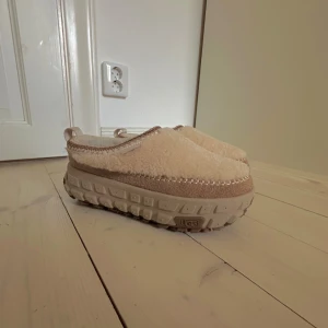 Beige UGG slip-ons, platå med teddyfoder - UGG slip-ons i beige med fluffigt teddyfoder och grov sula. Skorna har dekorativa sömmar runt öppningen och är tillverkade i syntet och mocka. Perfekta för dig som gillar chunky och mysiga skor med streetkänsla. Endast prövade aldrig använda. Nypris ca 2500 kr.
