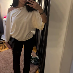 Vit offshoulder topp med vida ärmar - Säljer en vit offshoulder topp med vida trekvartsärmar. Toppens tyg är mjukt och har en lätt struktur, vilket ger en chill och avslappnad vibe. Passformen är loose och toppen sitter snyggt över ena axeln för en trendig look.