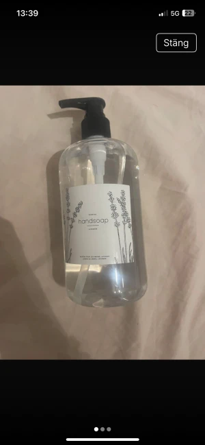 Lavendeldoftande handtvål med pump - En stor, transparent flaska med lavendeldoftande handtvål. Flaskan har svart pump och stilren vit etikett med lavendelillustrationer. Perfekt för badrum eller kök för en fräsch känsla och mjuka händer.