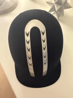 Svart ridhjälm med silvrig detalj - Säljer en svart ridhjälm från Lamicell med snygg silvrig U-formad metallist framtill. Hjälmen har klassisk form, justerbart hakband och mjuk vaddering på insidan för extra komfort. Nästan helt oanvänd, säljer pågrund av slutat med ridning. Inga andra defekter! Hjälmpåsen medföljer, pris kan diskuteras STORLEK: 55