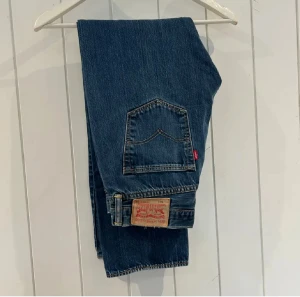 Levi's 501 mörkblå jeans straight fit - Klassiska Levi's 501 jeans i mörkblå tvätt med raka ben och normal passform. Byxorna har fem fickor, knappgylf och den ikoniska läderpatchen bak. Tillverkade i slitstarkt bomullsjeansmaterial med snygga kontrastsömmar och röd Levi's-tag på bakfickan. W33 och L32