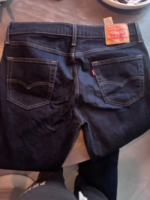 Levi's 502 mörkblå jeans W34 L30 - Säljer ett par Levi's 502 jeans i mörkblå tvätt med klassisk femficksdesign och kontrastsömmar. Modellen har rak passform och normal midja. Materialet är slitstarkt jeans och märkeslappen syns tydligt bak. Perfekt för dig som gillar tidlös stil.