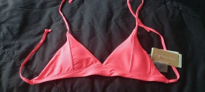 Neonrosa bikiniöverdel från Röhnisch - Snygg trekantsbikini i neonrosa från Röhnisch. Modellen har smala knytband i nacken och ryggen för justerbar passform. Perfekt för sommardagar på stranden. Tillverkad i ett mjukt och stretchigt syntetmaterial.