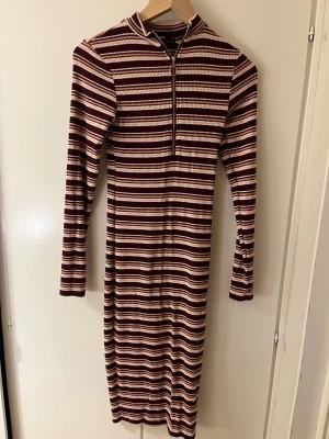 Randig långklänning från Bik Bok XS - Snygg långärmad långklänning från Bik Bok i storlek XS. Klänningen har ett randigt mönster i vinrött, beige och vitt, med ribbad struktur och en cool dragkedja framtill. Perfekt för dig som gillar retrovibbar och vill sticka ut med en unik look.