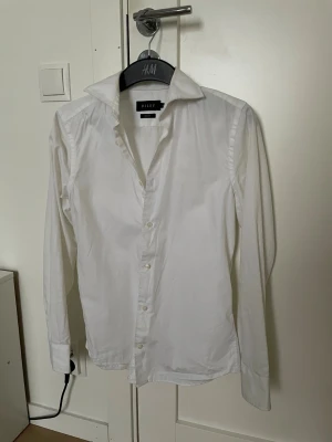 Vit slim fit skjorta från Riley XS - Klassisk vit skjorta från Riley i slim fit-modell. Skjortan har långa ärmar, krage och knäppning framtill. Perfekt för en clean och stilren look. Tillverkad i bomull för en skön känsla och snygg passform. I princip oanvänd! Bara att skriva om du har några frågor! 😇🙌