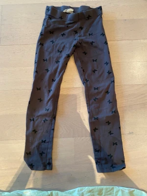 Grå leggings med fjärilsmönster H&M - Snygga grå leggings från H&M med svarta fjärilar över hela byxan. De är tillverkade i mjuk bomull och har en elastisk midja för skön passform. Perfekta för dig som gillar coola detaljer och mönster.