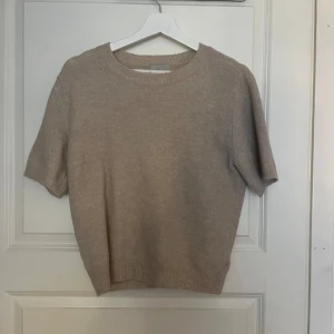 Beige stickad tröja med kort ärm - Säljer en enkel och stilren beige stickad tröja med korta ärmar och rund hals. Tröjan har ribbade muddar vid hals, ärmslut och nederkant. Använd 2/3 gånger så den är i väldigt fint skick 🤍