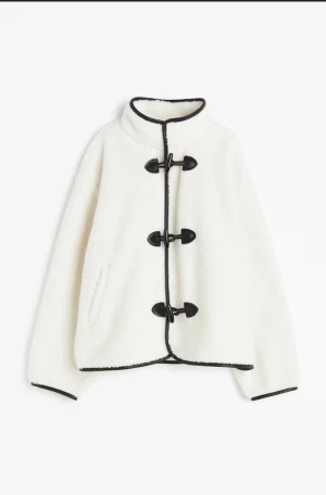 Vit pilejacka med svarta detaljer - Säljer en vit pilejavka med svarta kanter och snygga knäppningar framtill. Jackan har hög krage, lång ärm och en mysig, fluffig känsla. Från hm, köpt gör 550kr