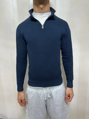 Marinblå stickad tröja med half zip - Snygg marinblå stickad tröja med half zip och hög krage. Tröjan har långärmade smala ärmar och ribbade muddar vid ärmslut och nederkant. Perfekt för dig som gillar stilrena och klassiska plagg med en modern touch.