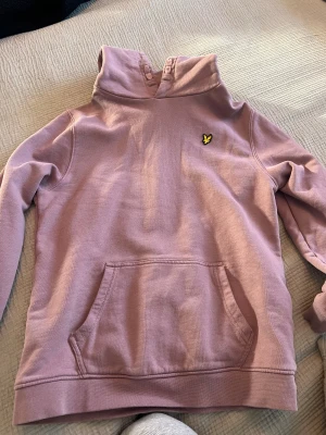 Ljuslila hoodie från Lyle & Scott - Säljer en ljuslila hoodie från Lyle & Scott med klassisk gul fågel-logga på bröstet. Tröjan har huva, magficka och långa ärmar. 