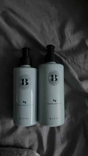 Björk Silver Shampoo & Conditioner - Två stilrena ljusgrå flaskor med svart pump från Björk, innehållande Ag Silver Shampoo och Silver Conditioner. Perfekt för dig som vill behålla kalla toner i håret. Flaskorna är gjorda av plast och har en modern, minimalistisk design. HELT OANDVÄNDA