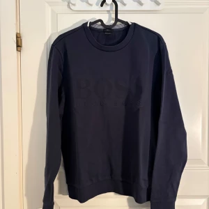 Mörkblå sweatshirt från BOSS - Säljer en mörkblå sweatshirt från BOSS med diskret logotyp på bröstet. Tröjan har rund halsringning och långa ärmar. Slim fit-modell som passar perfekt till vardags. Klassisk och stilren design.