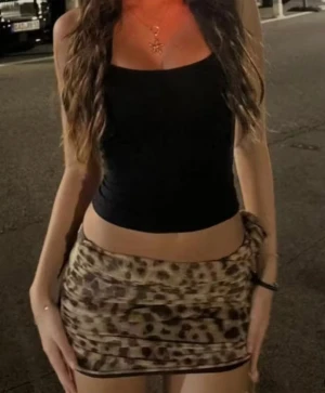 Leopardmönstrad kortkjol med knyt size M - Säljer en snygg kortkjol med leopardmönster i beige och bruna toner. Kjolen har en tight passform och coola rynkade detaljer på sidorna samt ett knytband för extra stil. Materialet är mjukt och stretchigt, perfekt för att skapa en trendig look.