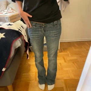 Blå bootcut jeans med låg midja - Snygga blå jeans med bootcut och låg midja. Jeansen har klassisk femficksdesign, slitningar framtill och bakfickor med broderad detalj. Perfekta för dig som gillar en avslappnad och trendig look.