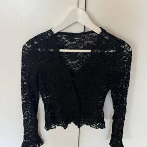 Svart spetsblus från Gina Tricot - Säljer en svart, långärmad spetsblus från Gina Tricot. Blusen är croppad med v-ringning och knappar framtill. Den har ett genombrutet spetsmönster. Använt enstaka gång, i nyskick!