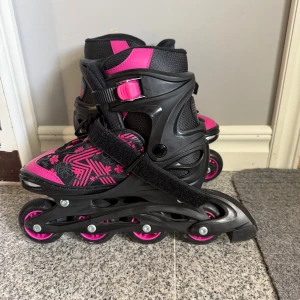 Svartrosa inlines från Roces stl 34-37 - Säljer ett par snygga inlines från Roces i svart och rosa med coola mönster och blommor. Skorna har justerbar storlek, robust plastskal och kardborreband för extra stöd. Perfekta för dig som vill rulla fram med stil i parken eller på gatan.