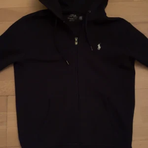 Svart hoodie från Polo Ralph Lauren XS - Använd kanske 5 gånger! Svart hoodie från Polo Ralph Lauren i storlek XS. Klassisk design med dragkedja framtill, huva med snörning och broderad logga på bröstet. Tillverkad i mjuk bomull och har långa ärmar samt fickor framtill.