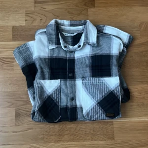 Svartvit rutig overshirt från H&M - Overshirt i svartvitt rutigt mönster från H&M. Skjortan har två stora bröstfickor med lock, knappar framtill och klassisk krage. Tillverkad i mjuk bomull och har långa ärmar med knapp vid ärmslut. Perfekt för lager-på-lager-stil. Tröjan är i storlek 164 cm vilket motsvarar xs-s. Tröjan är i väldigt fint skick. 