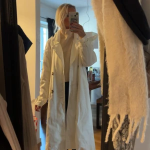 Vit trenchcoat  - Lång vit trenchcoat med både knappar och bälte! Perfekt för dig som vill ha en clean och stilren look under vår och höst.