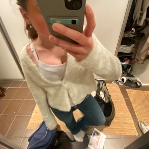 Vit fluffig kofta från Zara - Supermjuk och fluffig vit kofta från Zara med v-ringning och knappar framtill. Koftan har lång ärm och är i en stickad, lurvig kvalitet som känns riktigt cozy. Perfekt att slänga på sig över ett linne eller t-shirt.