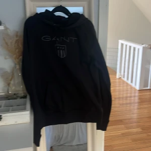 Svart hoodie från GANT med logga - Svart hoodie från GANT med stor logga och sköld på bröstet. 