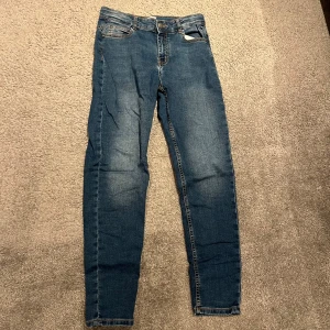 Blå skinny jeans från Only - Snygga blå skinny jeans från Only med klassisk femficksdesign och diskret slitning på låren. Jeansen har normal midja och är tillverkade i stretchigt denim för en bekväm passform. Perfekta för dig som gillar en smal siluett och enkel stil. Passar dig som är ungefär 155-160 beroende på hur mycket du väger. Du kan också justera hur tajt midjan ska vara med hjälp av knapparna som sitter innanför byxan.