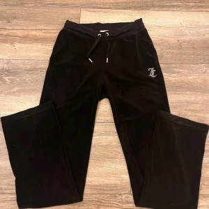 Svarta velourbyxor Juicy Couture XS - Svarta mjukisbyxor från Juicy Couture i glansig velour med snörning i midjan och silverfärgad logga framtill. Baktill står det 'Juicy' i glittriga stenar. Dock har mycket glittriga stenar lossnat, nypris ca 1200kr men sänks mycke pga av stenarna. Går även att köpa hela setet och pris kan diskuteras