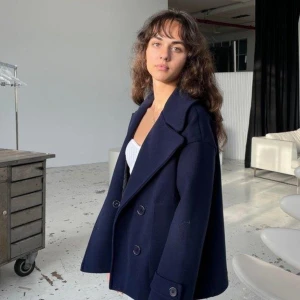 Mörkblå skepparkavaj från design by si - Stilren mörkblå skepparkavaj med dubbelknäppning och stora slag. Jackan har en klassisk, rak passform och är tillverkad i ett tjockare material som passar perfekt för kyligare dagar. Snygga knappar framtill och vid ärmsluten ger en tidlös look.