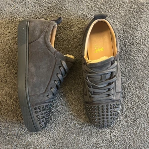 Christian Louboutin  - Säljer ett par gråa Christian Louboutin i mocka med ikoniska röda sulor. Skorna har rund tå, snörning och nitar framtill. Perfekta för dig som vill sticka ut med lyxiga detaljer och snygg design. Skobox medföljer.