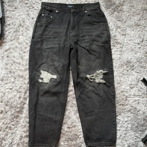 Svarta jeans med slitningar UnBlank M - Svarta baggy jeans med nice passform från UnBlank i modell med raka ben och coola slitningar på båda benen. Jeansen har klassisk femficksdesign och är tillverkade i denim. Perfekta för dig som gillar en avslappnad och trendig look.