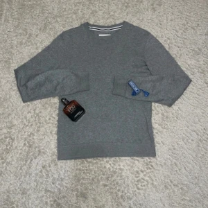 Grå stickad tröja från Pier One - Snygg grå stickad tröja från Pier One med rund hals och diskret vit och svart rand på insidan av kragen. Tröjan har långärmad passform och är perfekt för dig som gillar enkel och stilren design. Materialet är mjukt och bekvämt.