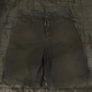 Svarta shorts från Billabong med tryck - Svarta shorts från Billabong i 100% bomull. De har klassisk femficksdesign, knapp och dragkedja fram samt coolt tryck med rutor och örn på ena bakfickan. Passar dig som gillar street och skate. Snygga detaljer och skön passform.