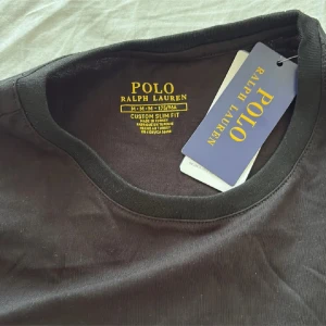 Svart t-shirt från Polo Ralph Lauren - Svart t-shirt från Polo Ralph Lauren i slim fit-modell. Klassisk rund halsringning och korta ärmar. Ikoniska broderade loggan i vitt på bröstet. Tillverkad i mjuk bomull för en skön känsla. Perfekt basic med stilren look.