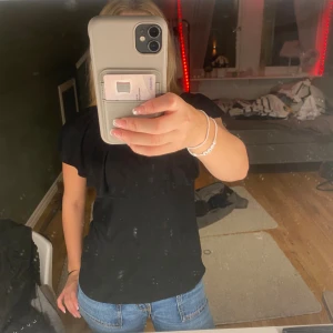 Svart ribbad topp med volang - Svart ribbad topp med bred volang över axlarna och rund halsringning. Toppen är ärmlös och har en mjuk, stretchig känsla. Perfekt att styla med jeans eller kjol för en chill look.