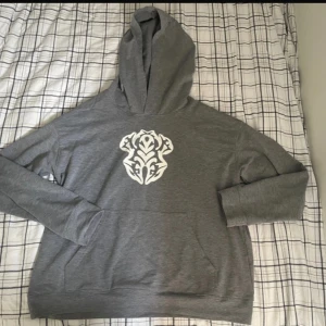 Grå hoodie med vitt tryck - Säljer en grå hoodie med ett stort vitt tryck  tryck på bröstet. Tröjan har huva, lång ärm och en klassisk känguruficka framtill. Perfekt för dig som gillar streetstyle och vill ha en chill look.