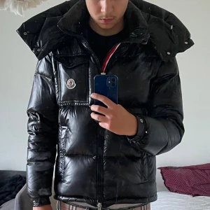 Svart pufferjacka från Moncler - Säljer en svart pufferjacka från Moncler med glansig finish och stor huva. Jackan har dragkedja framtill, bröstficka med Moncler-logga och flera praktiska fickor. Perfekt för kalla dagar och riktigt snygg till streetwear-stilen. Pris kan diskuteras 