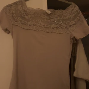 Beige spetströja från H&M - Supersöt beige tröja från H&M i storlek S. Tröjan har korta ärmar och en bred spetsdetalj över axlar och bröst som ger en romantisk vibe. Perfekt för dig som gillar stilrena och feminina plagg med extra detaljer! Går ej att köpa längre då den är ifrån vintage H&M
